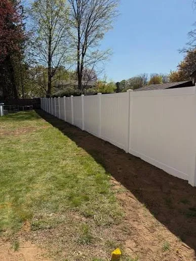 White vinyl privacy fence with posts installed along property line with mulch base
