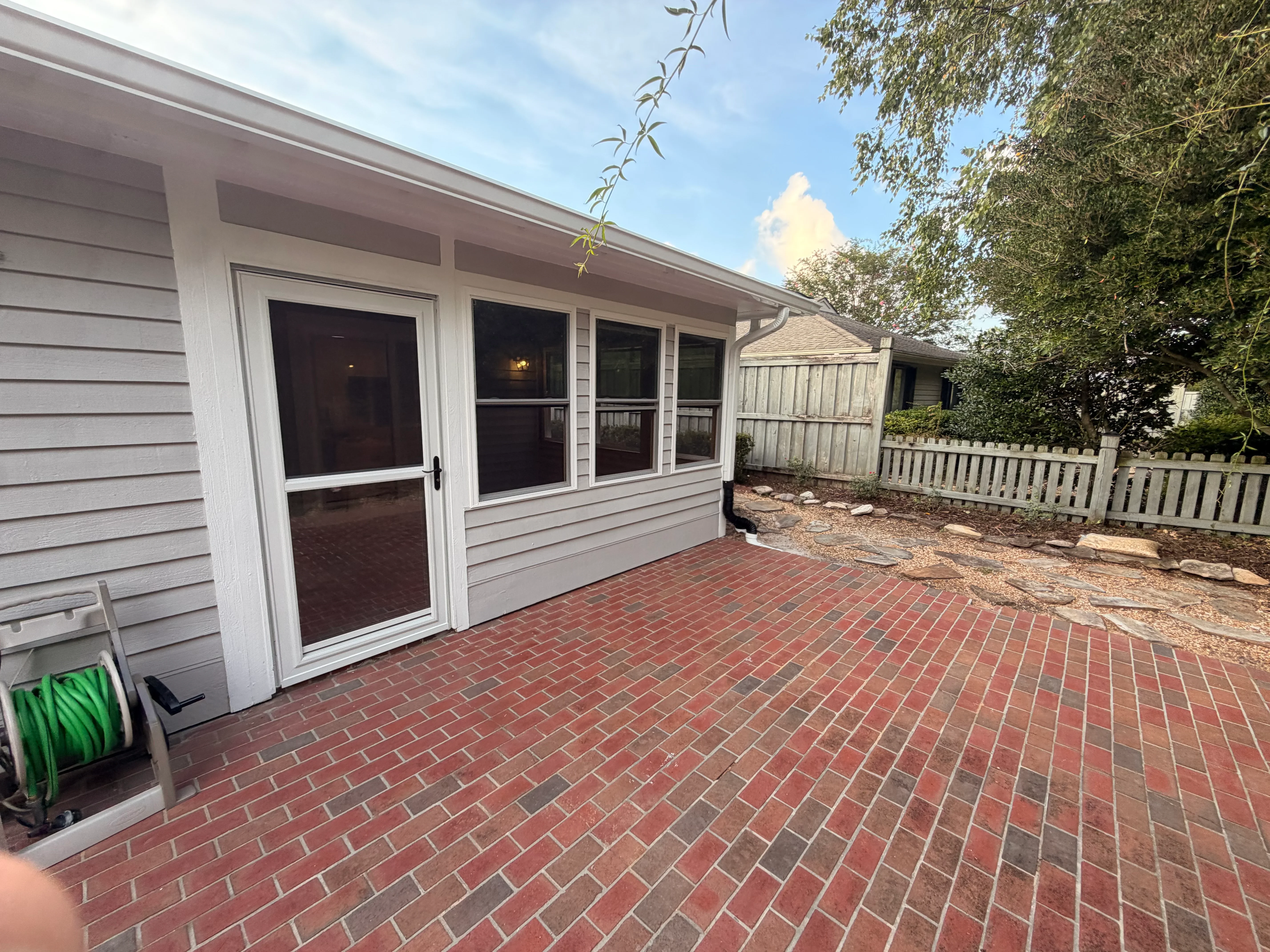 Vinyl sunroom with sliding glass windows and door on brick patio with white picket fence