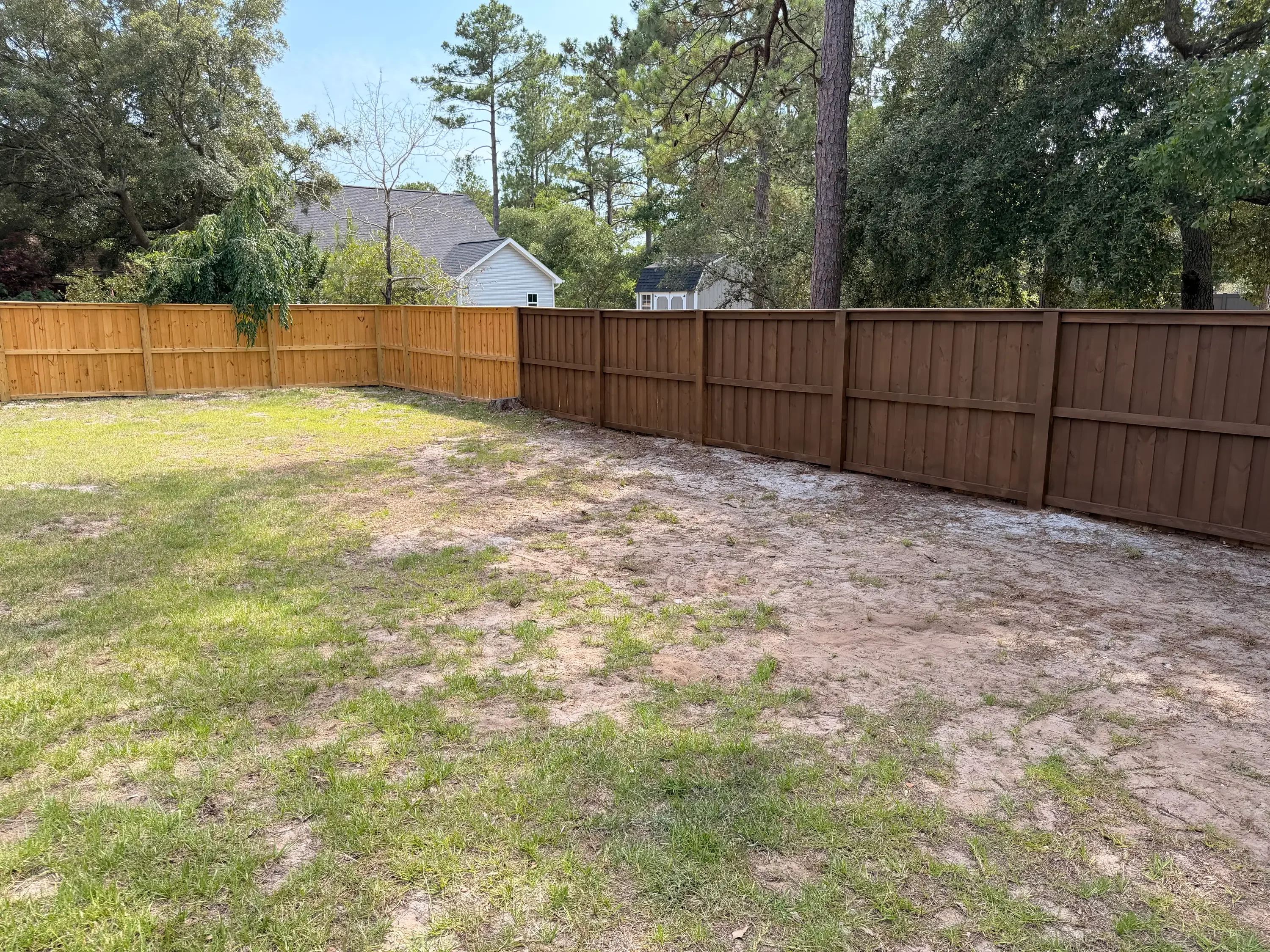 Cedar and stained wood privacy fence installation in residential backyard with vertical board construction