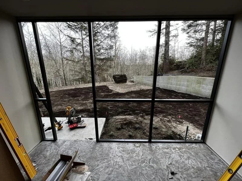 Interior sunroom with black-framed glass panels overlooking forest landscape