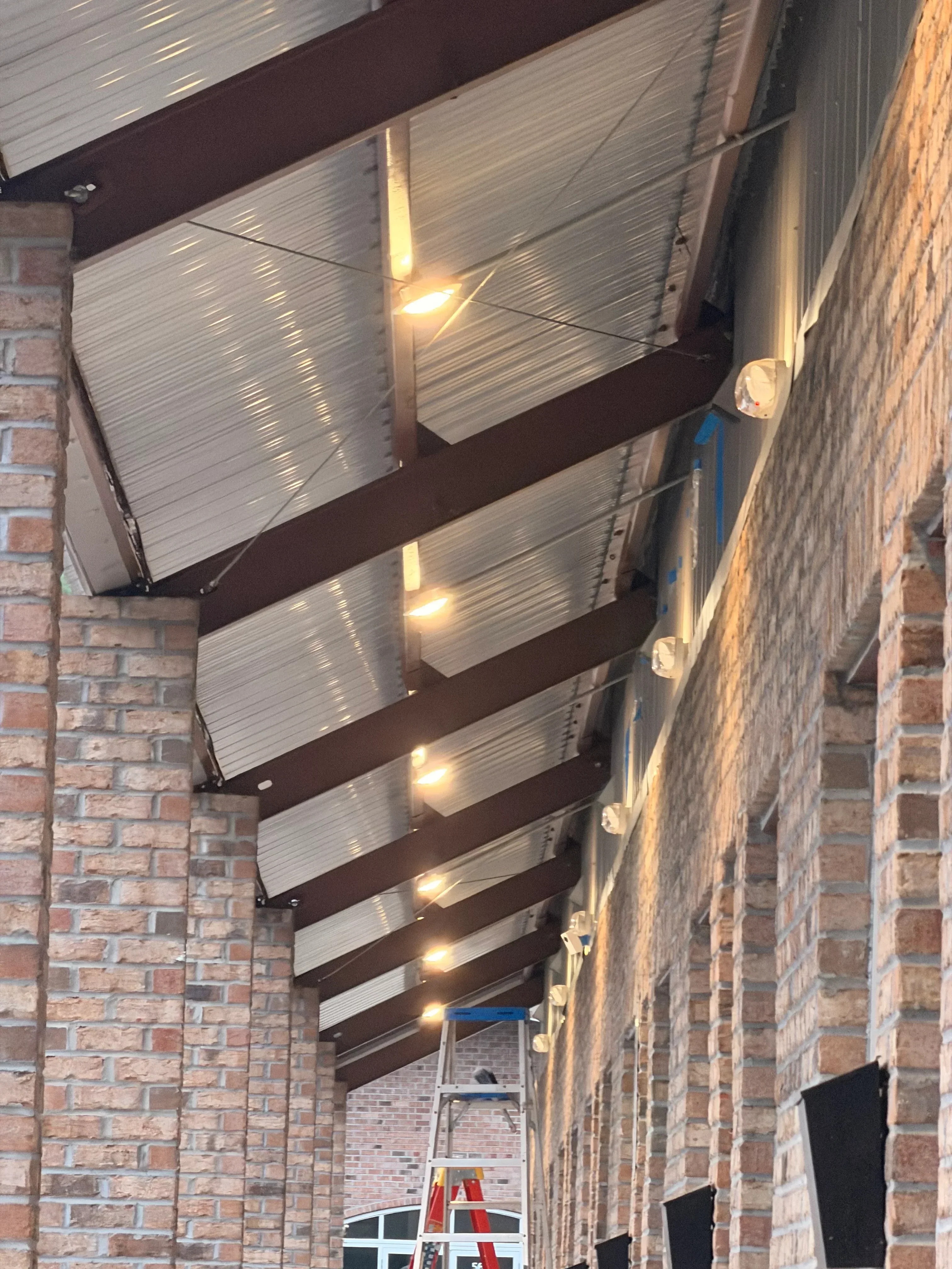 Metal corrugated awning panels with LED lights and steel support brackets on brick building
