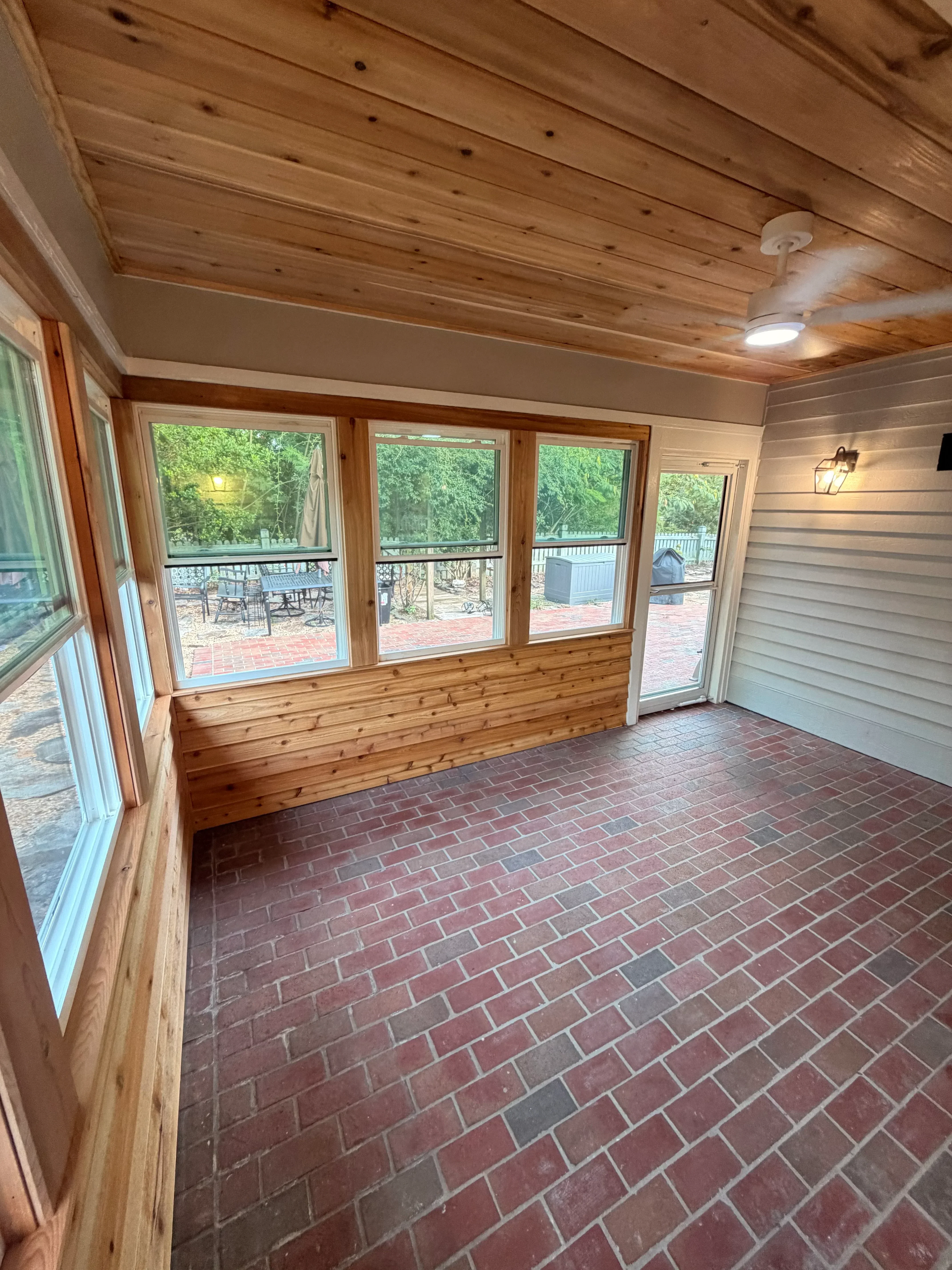 Interior sunroom with vertical wood paneling, multi-pane wooden windows, and brick accent wall
