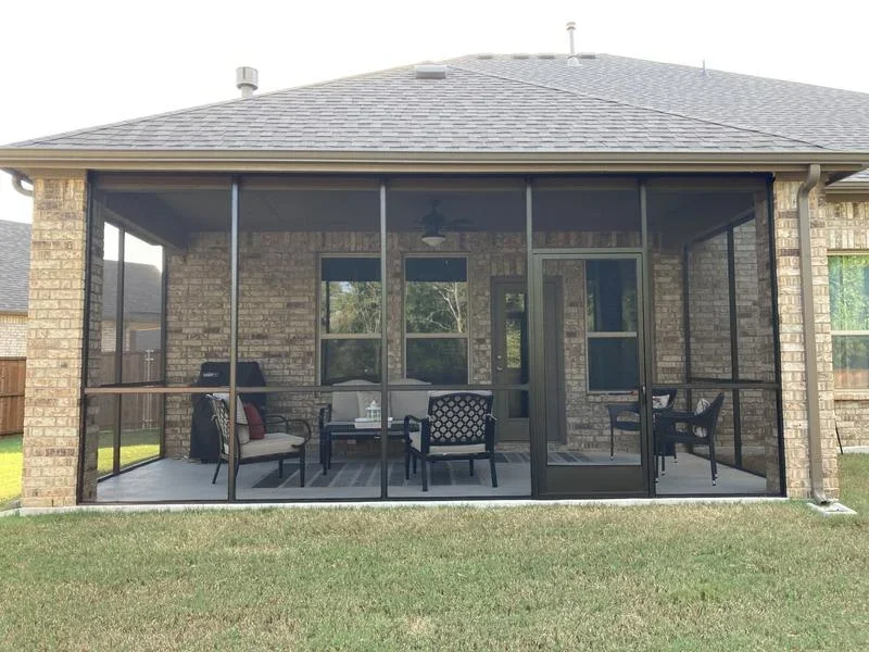 Aluminum screen patio enclosure with multiple panels and glass doors on brick home